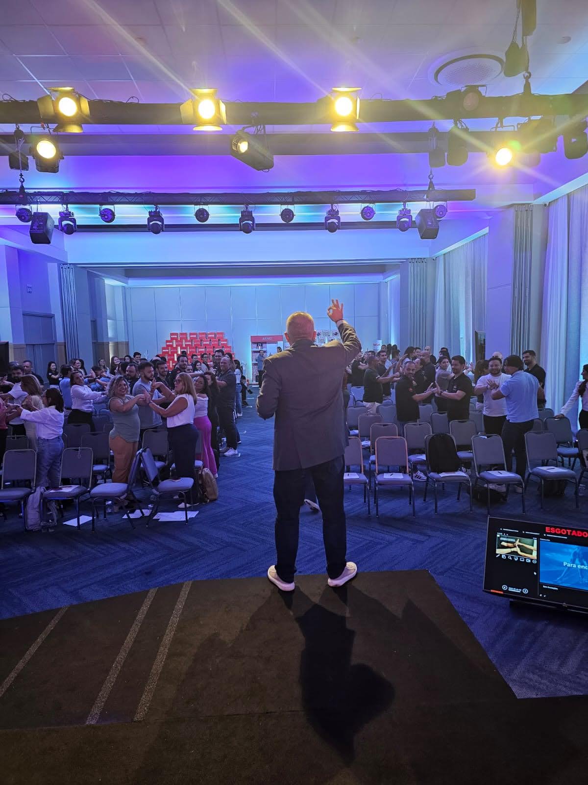 Rogério Chelucci de costas no palco conduzindo dinâmica com plateia em pé